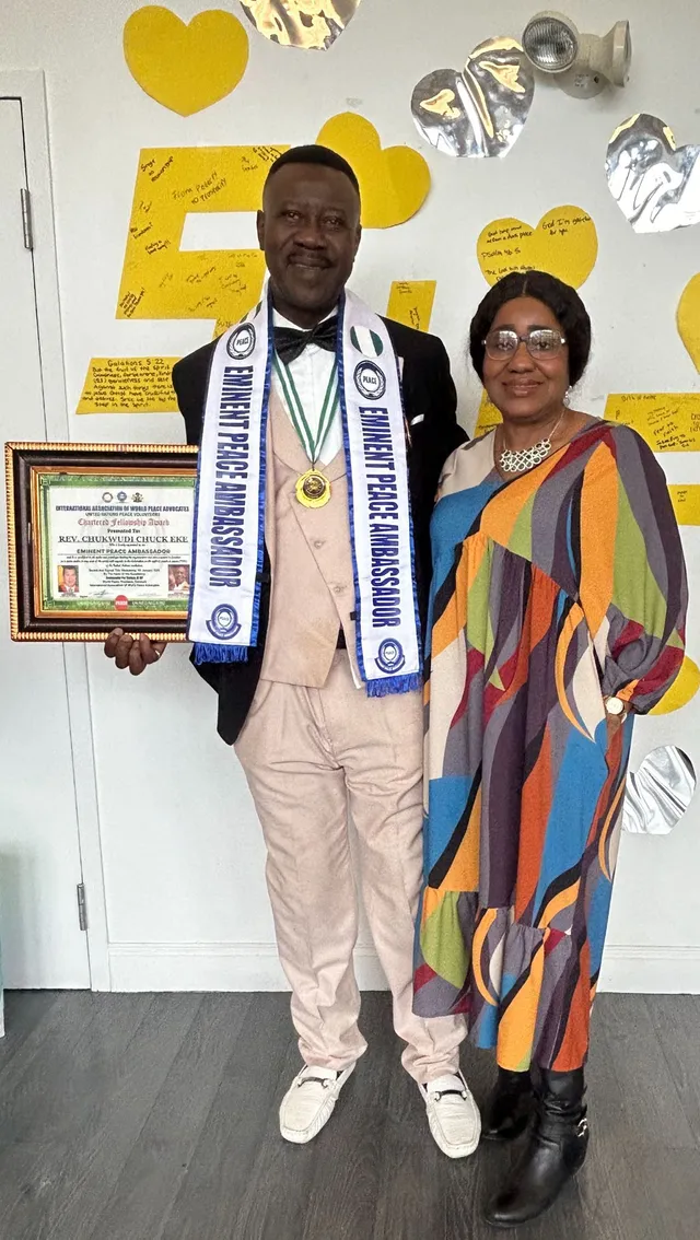 Chuck Eke wearing an Eminent Peace Ambassador sash and holding his framed IAWPA Chartered Fellowship Award certificate, standing beside another attendee at the ceremony
